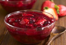 Beerengrütze in einer Glasschüssel auf einem Holztisch. Daneben ein Holzlöffel und geschnittene Erdbeeren