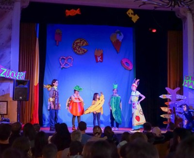 Children in vegetable and fruit costumes on stage, wearing bananas, tomatoes and cucumbers