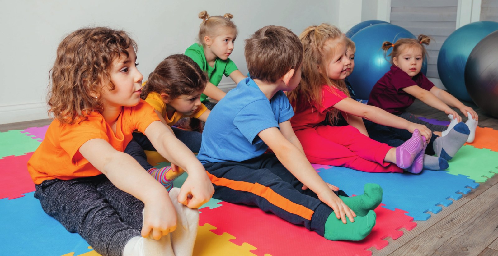 Eine Gruppe von Kita-Kindern sitzt auf bunten Gymnastikmatten und macht gemeinsam Dehnübungen.