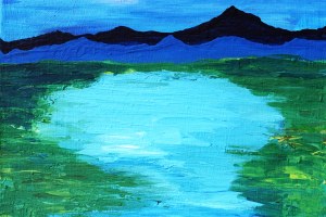 Blauer See mit grünem Ufer, in der Ferne verblauen die die Berge.